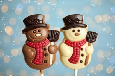 Funny chocolate snowmen candies against blurred festive lights, closeup