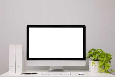 Photo of Comfortable workplace with blank computer display and plant on desk near light grey wall. Space for text