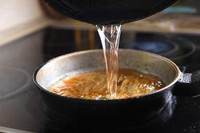 Pouring used cooking oil onto frying pan on stove