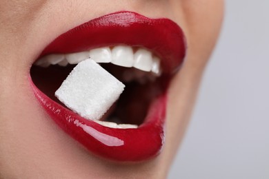 Closeup view of young woman with beautiful lips eating sugar cube on light grey background