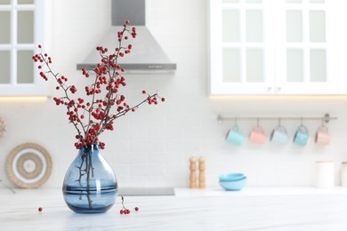 Photo of Hawthorn branches with red berries on table in kitchen, space for text