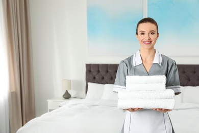 Photo of Chambermaid with stack of fresh towels in hotel room. Space for text