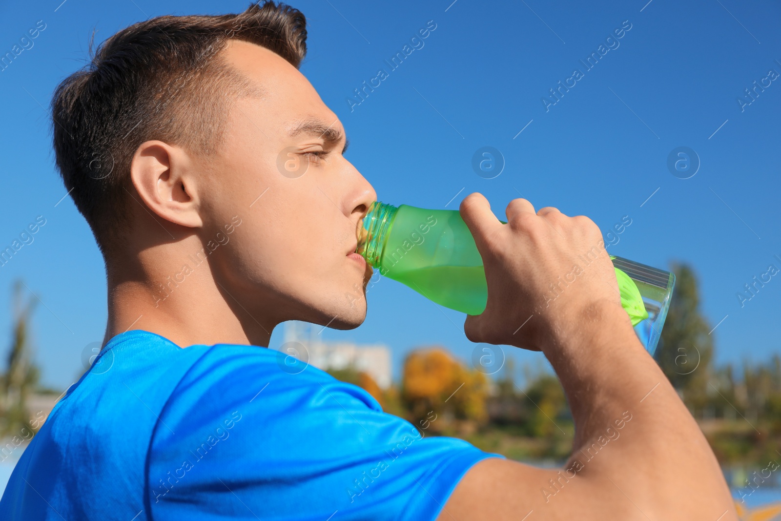 Photo of Young sporty man drinking water from bottle outdoors on sunny day