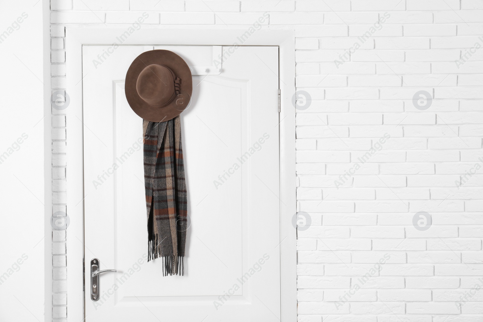 Photo of Hat and scarf hanging on white wooden door. Space for text