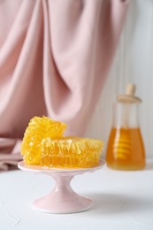 Photo of Stand with natural honeycombs and honey on white table, selective focus. Space for text