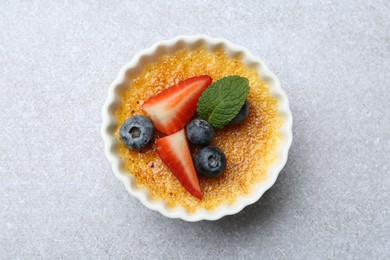 Delicious creme brulee with berries and mint in bowl on grey textured table, top view