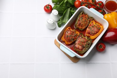 Photo of Tasty stuffed peppers in dish and ingredients on white tiled table, flat lay. Space for text