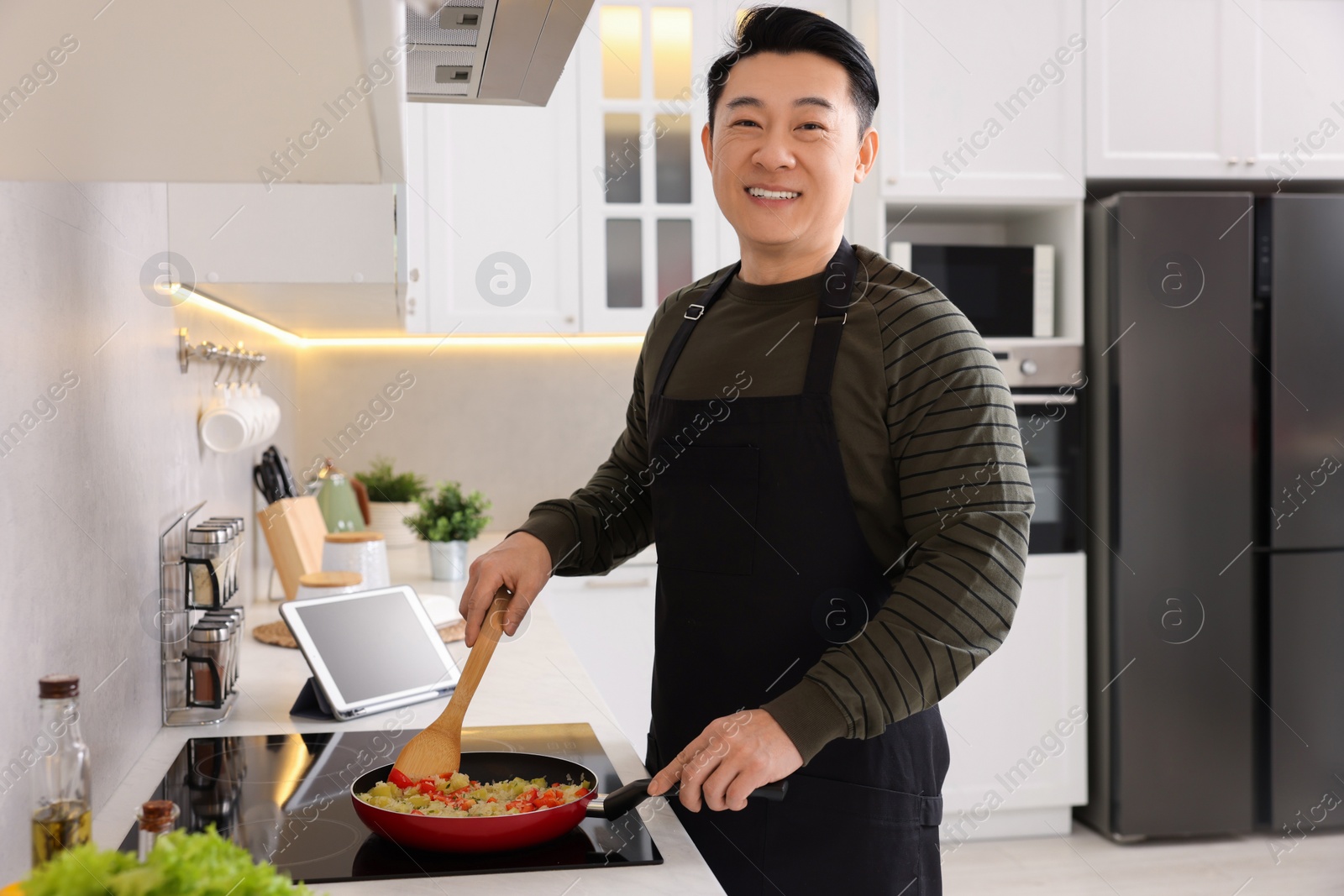 Photo of Happy man cooking dish on cooktop in kitchen