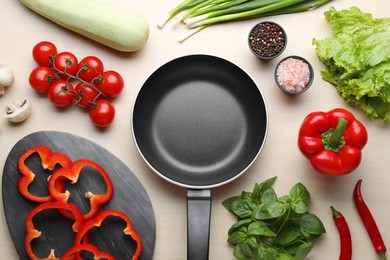 Photo of Empty frying pan, fresh vegetables and spices on wooden table, flat lay