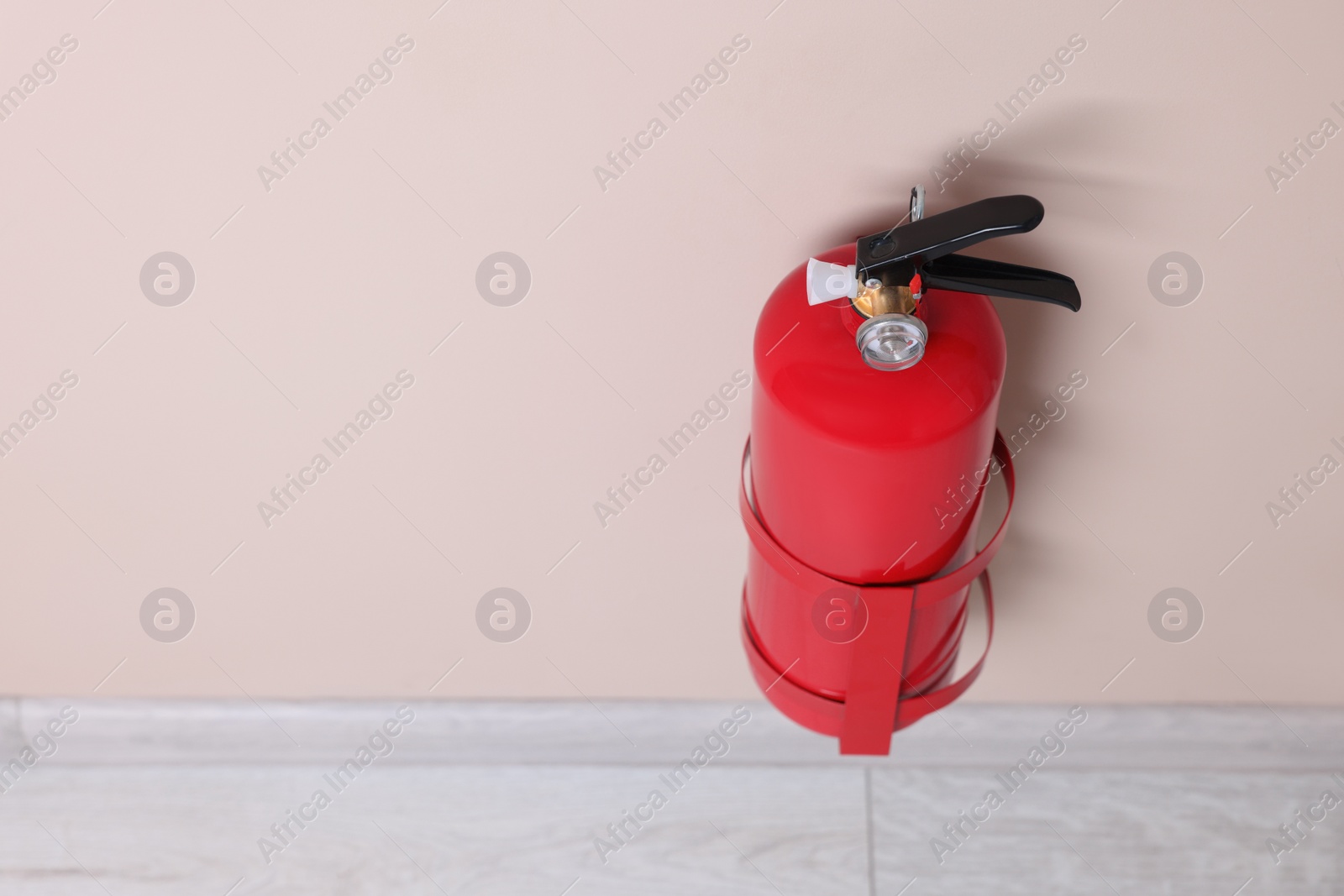 Photo of One fire extinguisher on beige wall, space for text