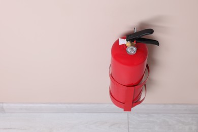 Photo of One fire extinguisher on beige wall, space for text