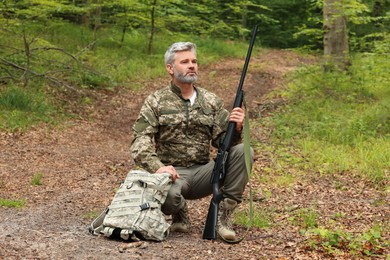 Man with hunting rifle and backpack wearing camouflage in forest