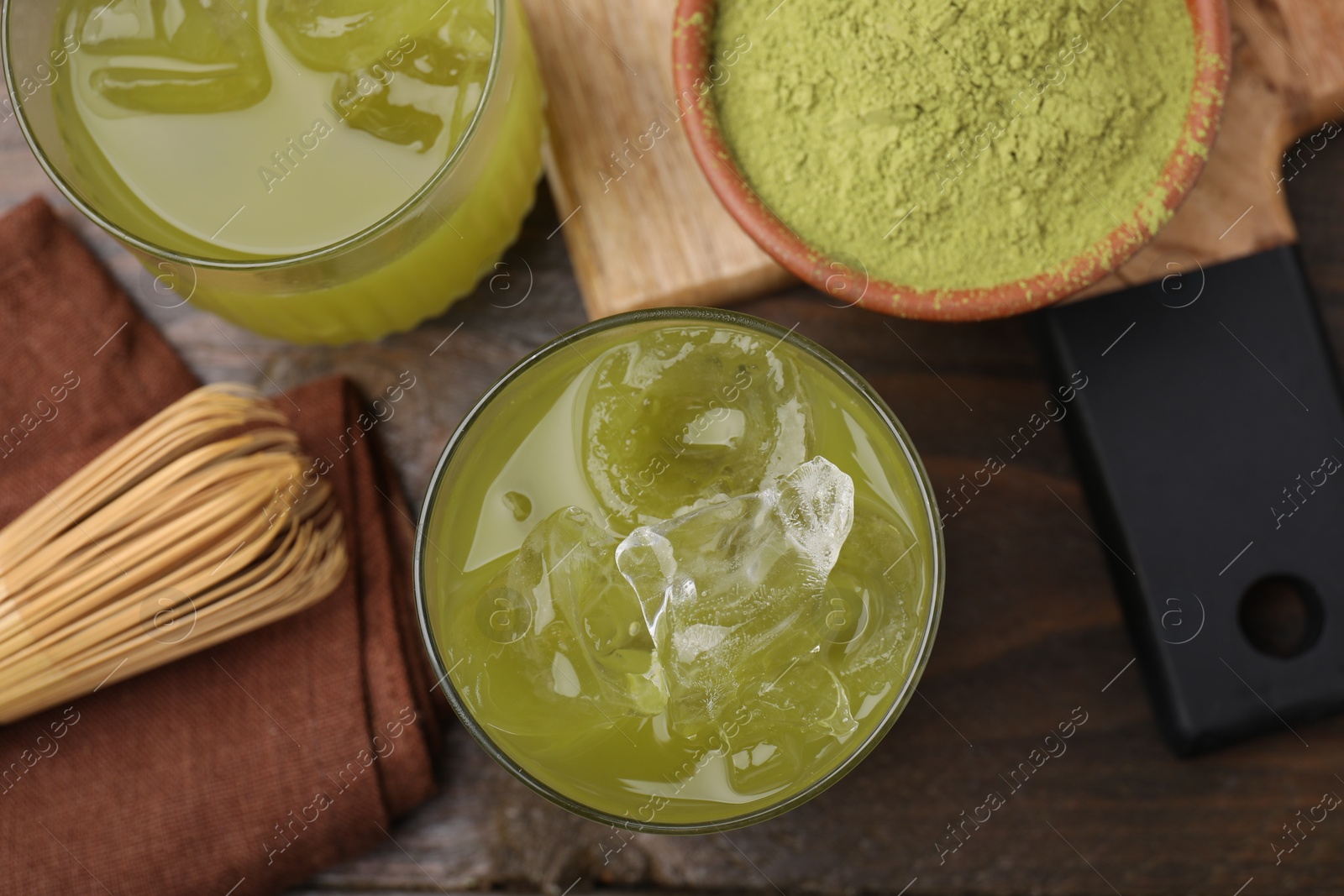 Photo of Delicious iced green matcha tea, powder and bamboo whisk on wooden table, flat lay