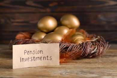 Photo of Many golden eggs and card with phrase Pension Investments on wooden table, space for text