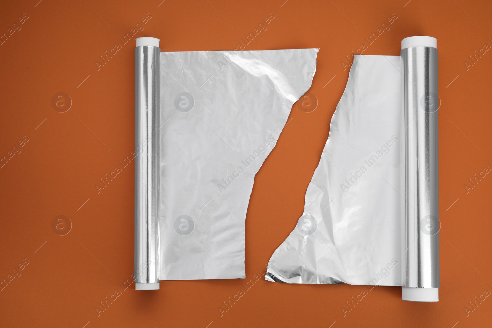 Photo of Rolls of aluminum foil on brown background, flat lay