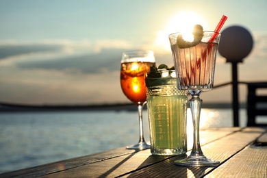 Glasses of fresh summer cocktails on wooden table outdoors at sunset, low angle view. Space for text