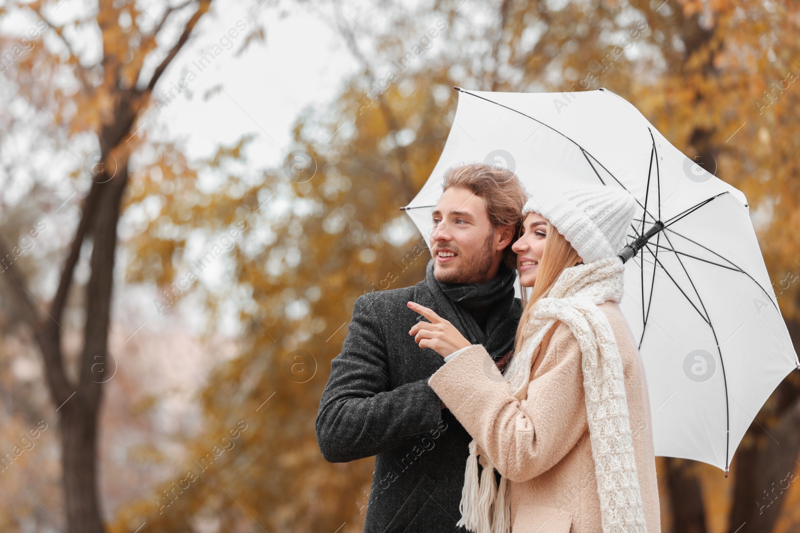 Photo of Young romantic couple with umbrella in park on autumn day