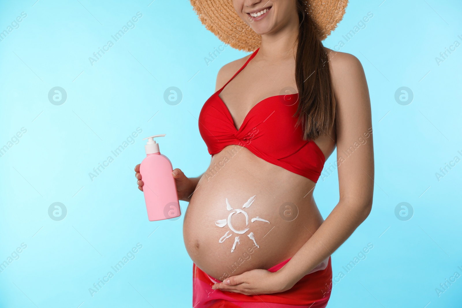 Photo of Young pregnant woman with sun protection cream on light blue background, closeup
