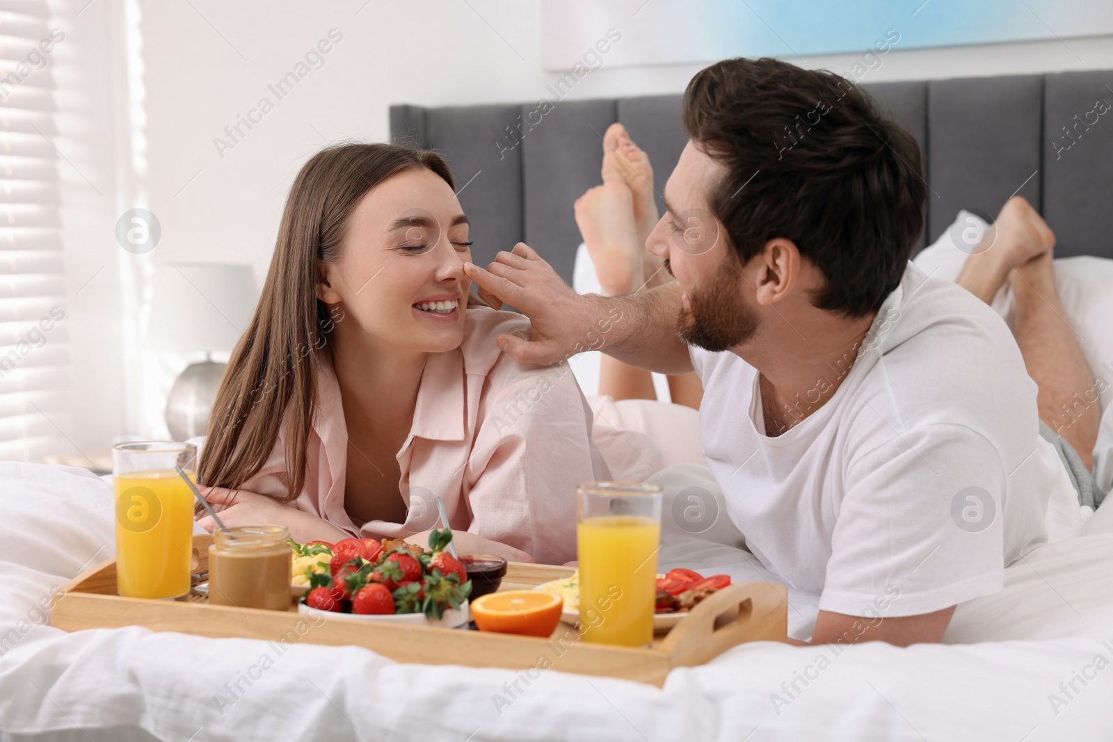 Photo of Happy couple eating tasty breakfast on bed at home