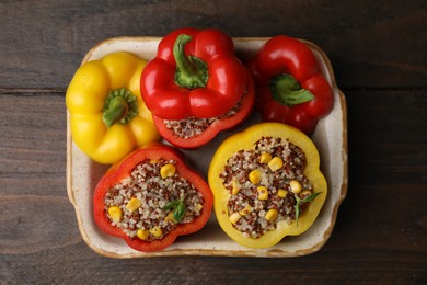 Photo of Quinoa stuffed bell peppers and basil in baking dish on wooden table, top view