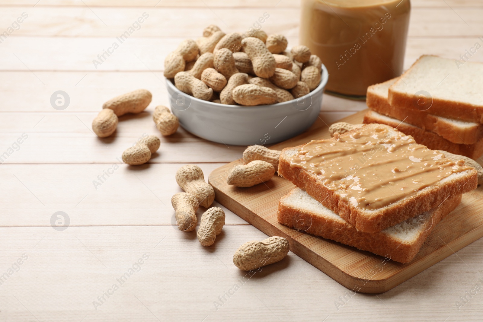 Photo of Delicious toasts with peanut butter and nuts on light wooden table, space for text