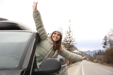 Happy woman leaning out of car window on road. Winter vacation