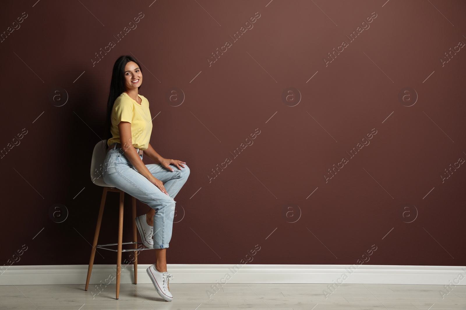 Photo of Beautiful young woman sitting on stool near brown wall. Space for text