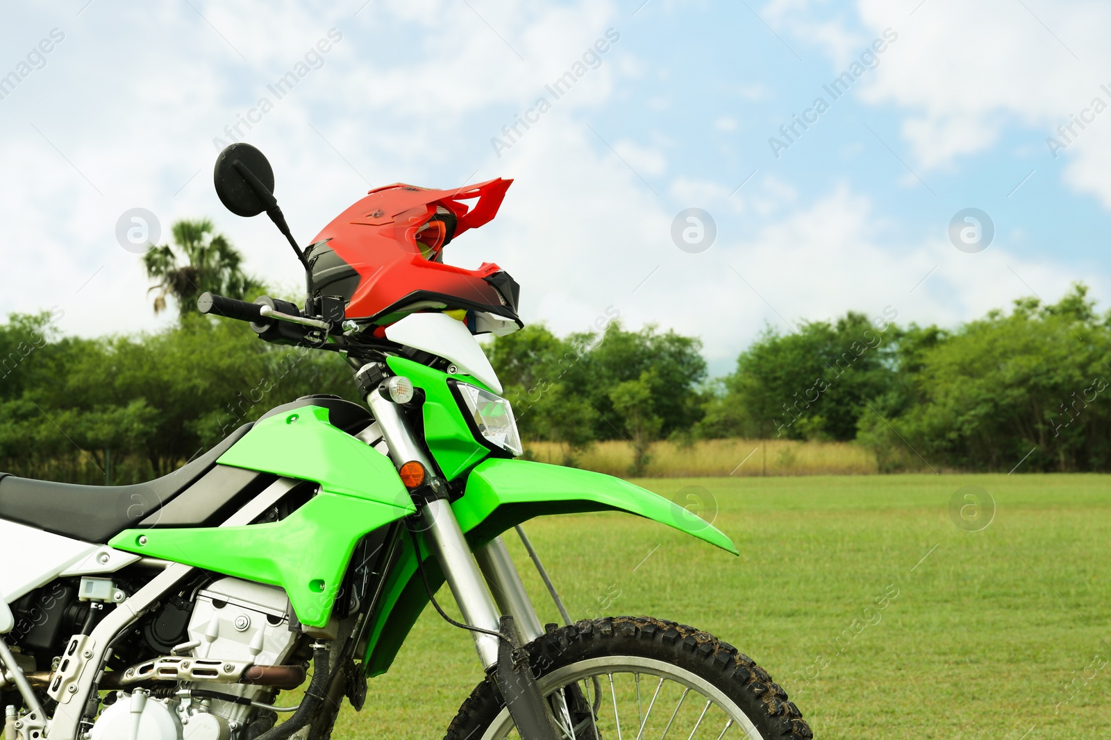 Photo of Stylish green cross motorcycle with helmet outdoors, space for text