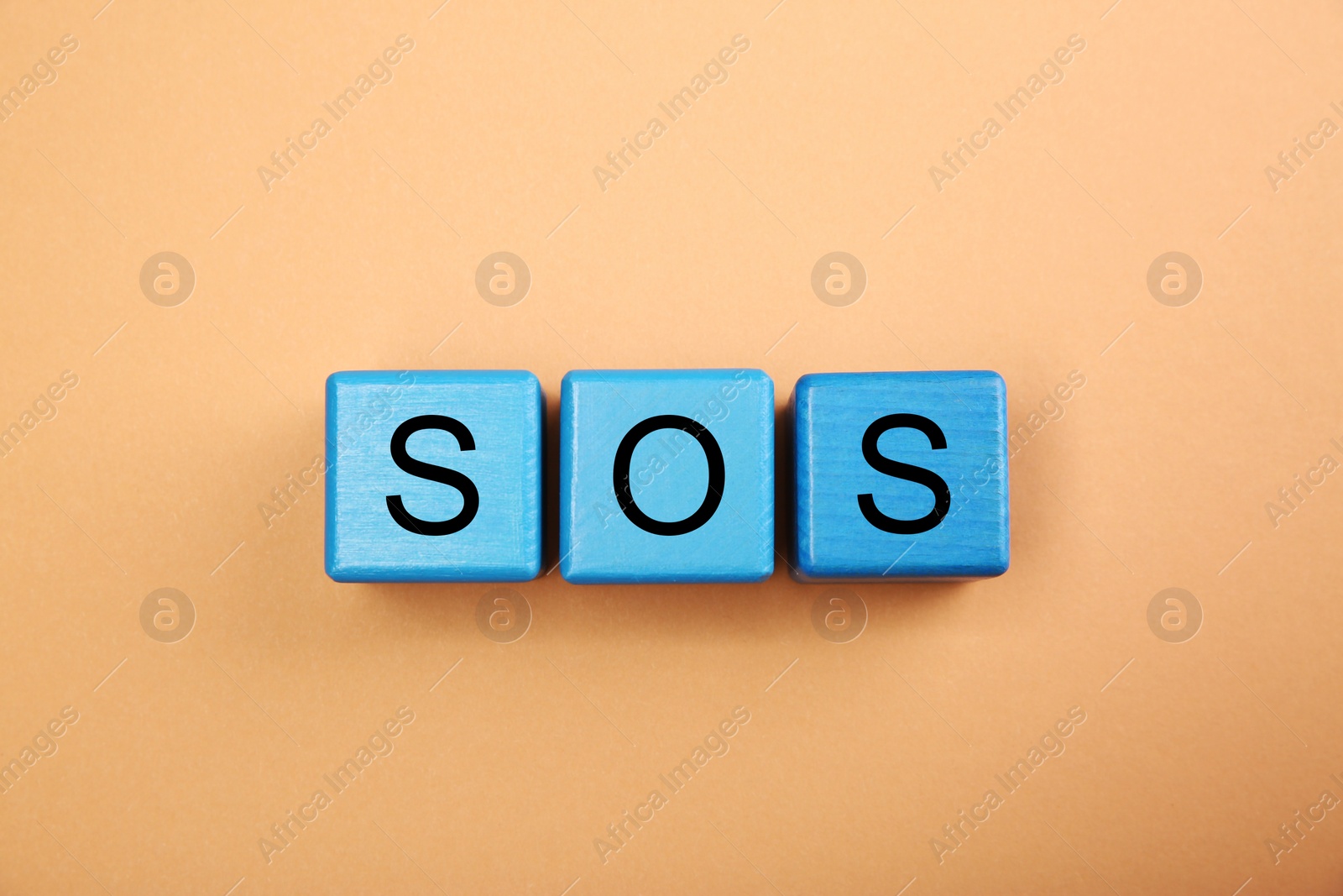 Photo of Abbreviation SOS (Save Our Souls) made of light blue cubes with letters on pale coral background, top view