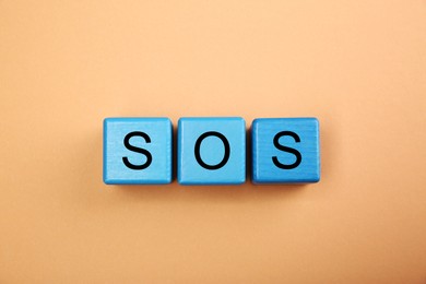 Abbreviation SOS (Save Our Souls) made of light blue cubes with letters on pale coral background, top view