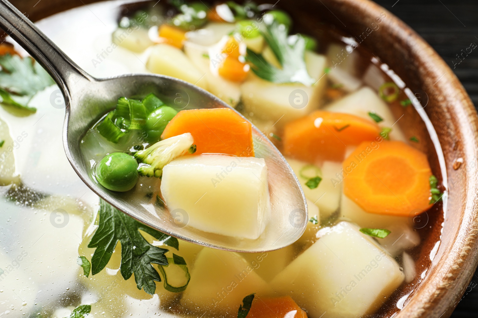 Photo of Spoon of fresh homemade vegetable soup over full bowl, closeup