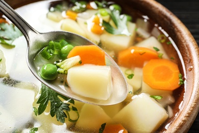 Spoon of fresh homemade vegetable soup over full bowl, closeup