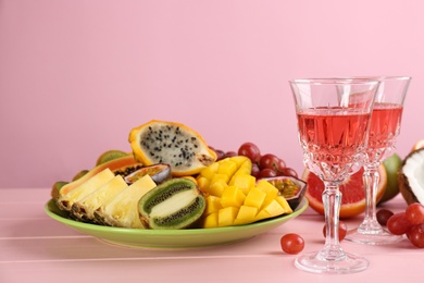 Photo of Delicious exotic fruits and glasses of wine on pink wooden table