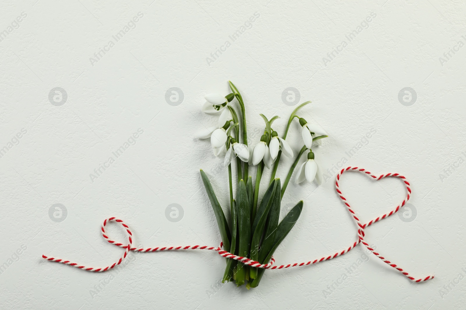 Photo of Beautiful snowdrops with traditional cord martisor on white background, flat lay and space for text. Symbol of first spring day