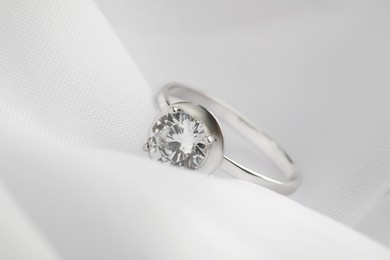 Photo of Beautiful engagement ring on white fabric, closeup