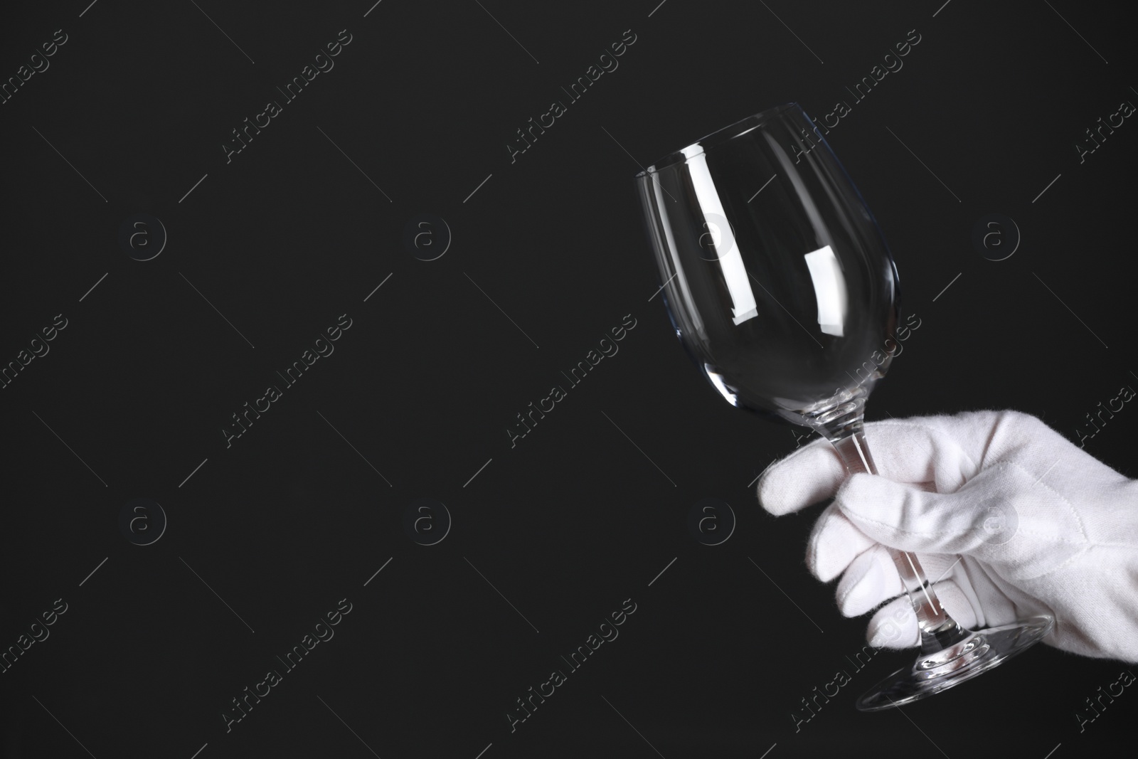Photo of Person in white glove checking cleanliness of glass on dark background, closeup. Space for text