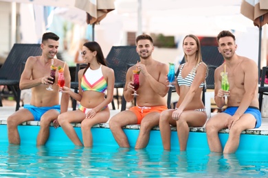 Happy young friends with refreshing cocktails near swimming pool