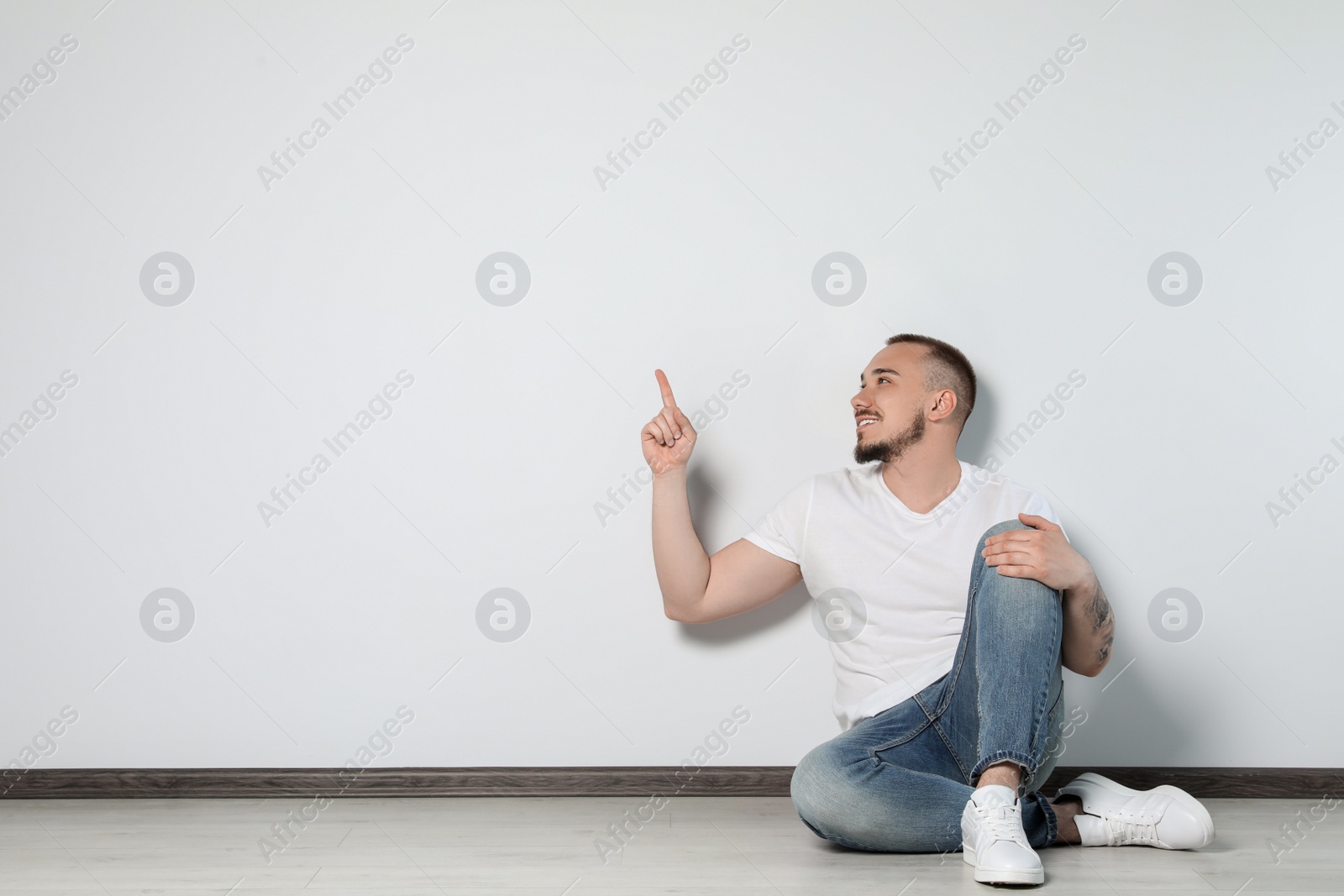 Photo of Handsome young man sitting on floor near white wall indoors, space for text