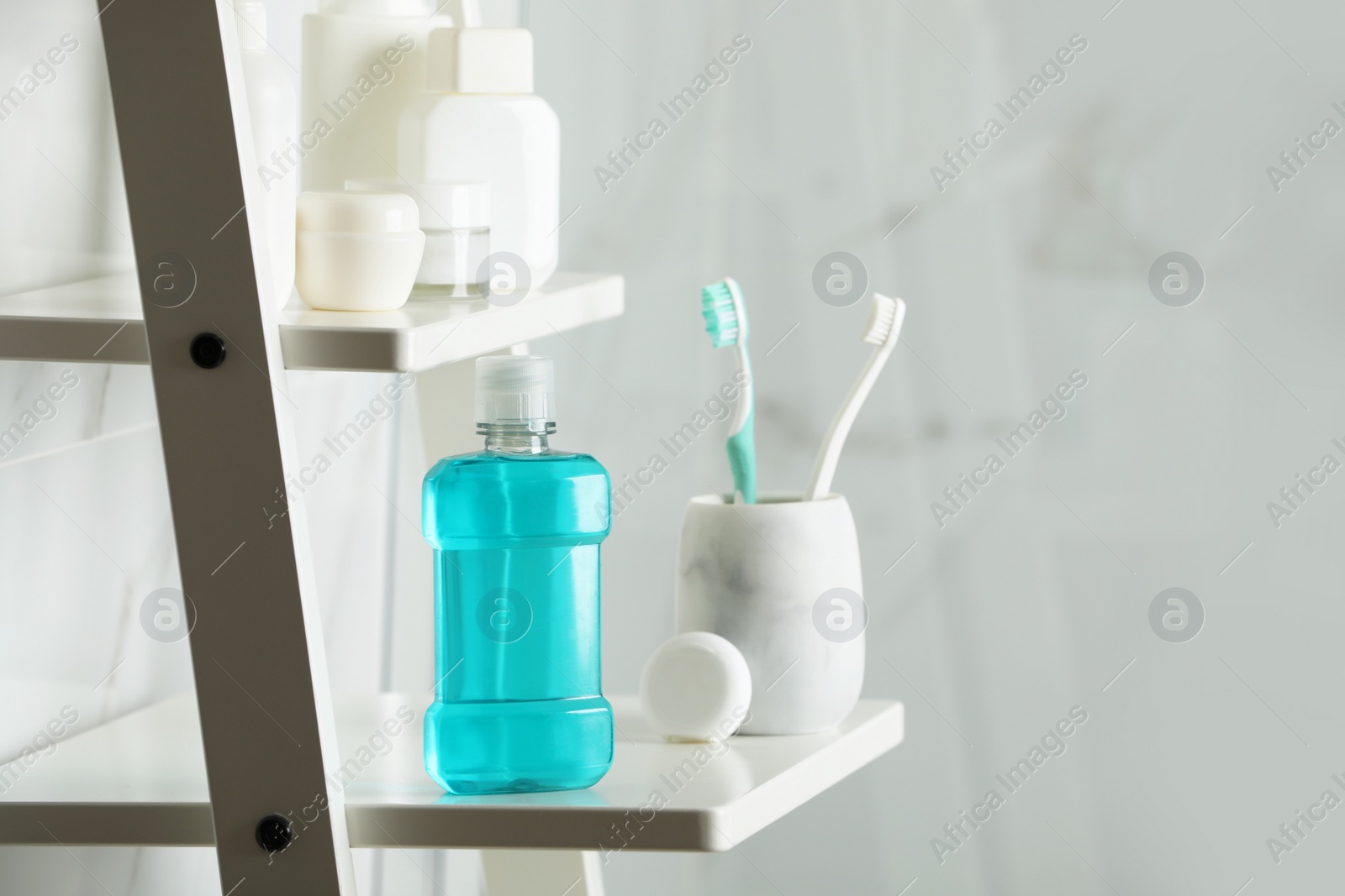 Photo of Bottle of mouthwash, toothbrushes and dental floss on white shelf in bathroom