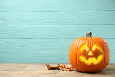 Photo of Scary jack o'lantern pumpkin on light blue wooden background, space for text. Halloween decor