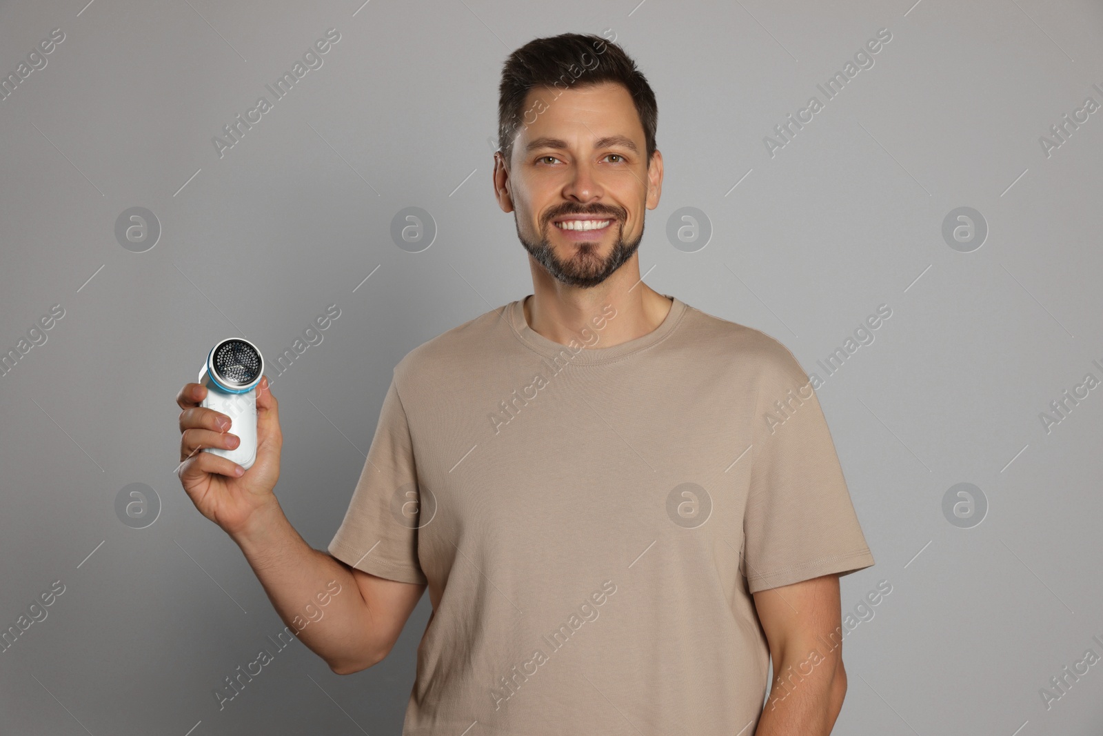 Photo of Handsome man holding fabric shaver on light grey background