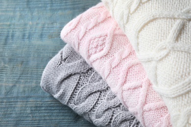 Photo of Stack of knitted sweaters on blue wooden table, closeup