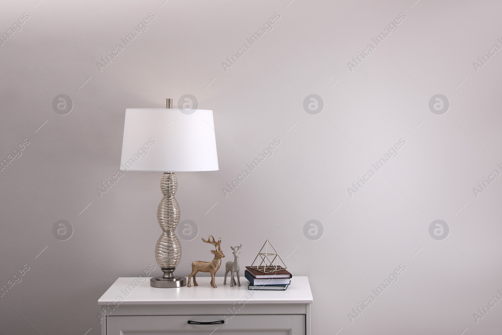 Photo of Wooden nightstand with books, decor and lamp near light wall in room, space for text