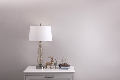 Photo of Wooden nightstand with books, decor and lamp near light wall in room, space for text