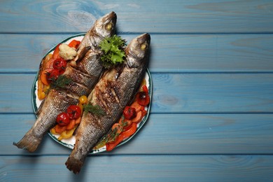 Photo of Plate with delicious roasted sea bass fish and vegetables on light blue table, top view