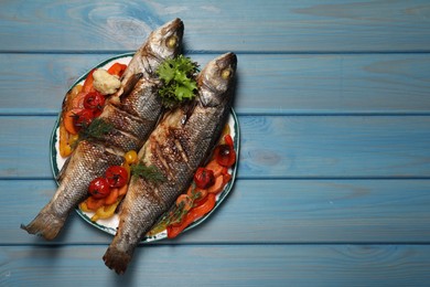 Plate with delicious roasted sea bass fish and vegetables on light blue table, top view