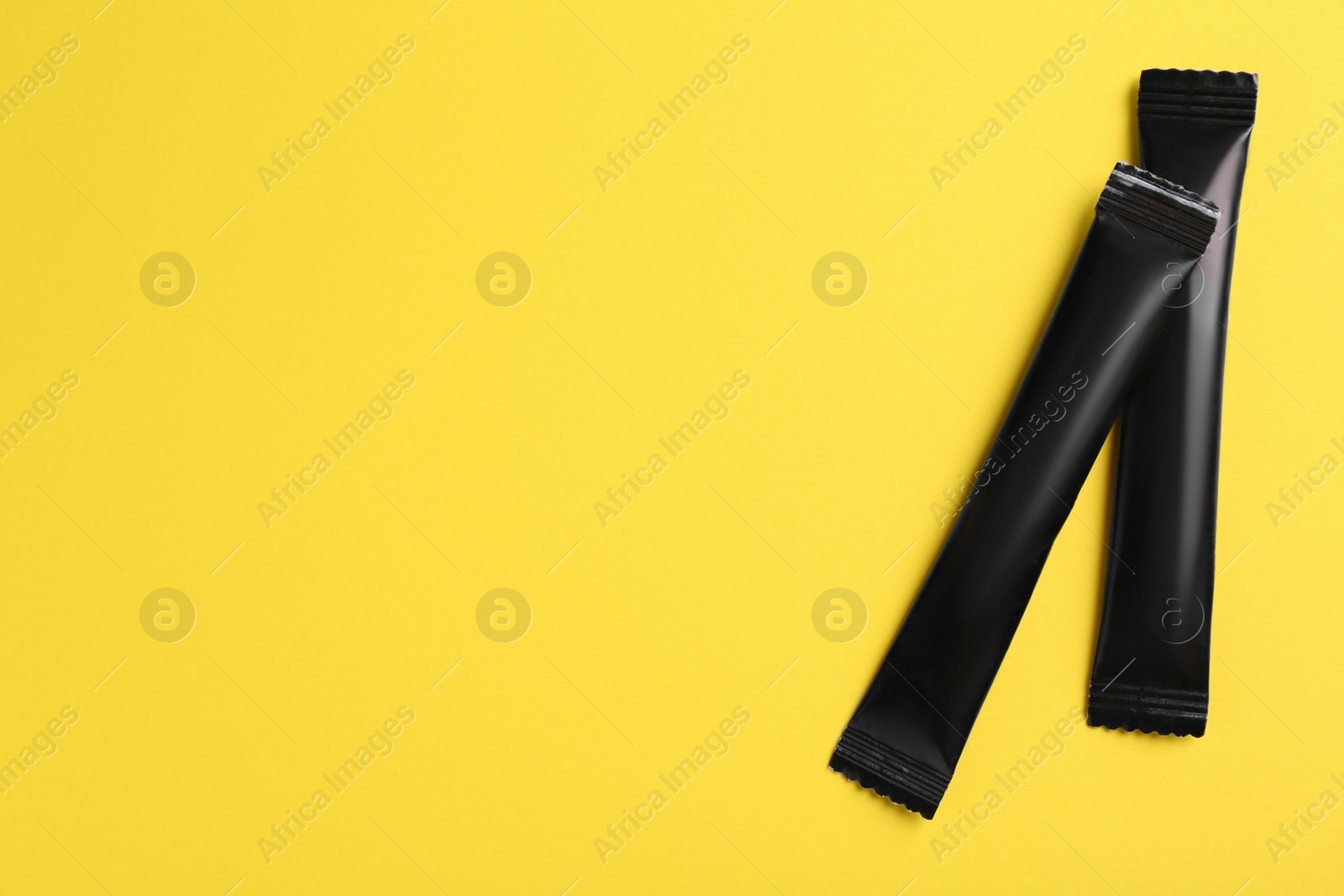 Photo of Black sticks of sugar on yellow background, flat lay. Space for text