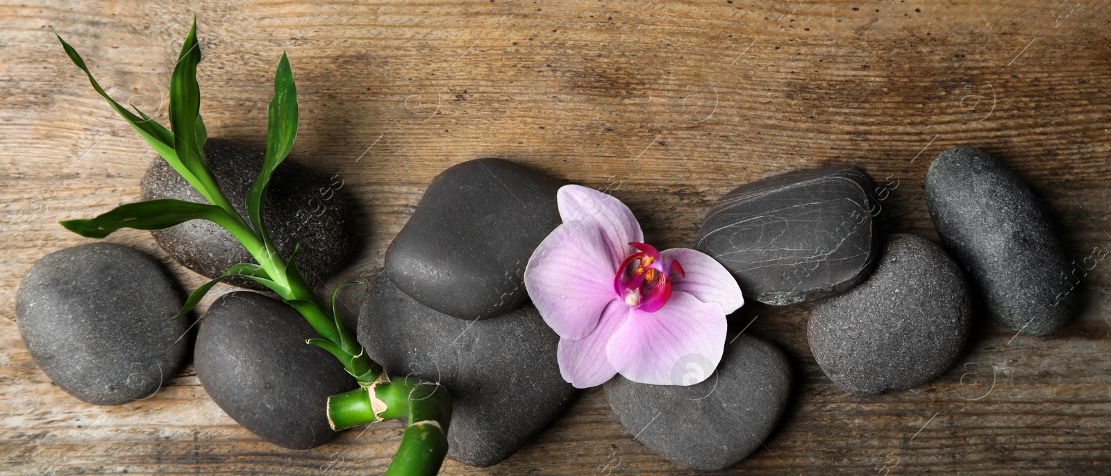 Image of Spa treatment. Flat lay composition with stones, bamboo and orchid flower on wooden table. Banner design