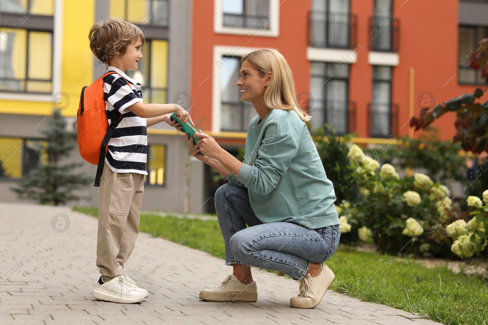 Photo of Happy woman giving notebook to her son near kindergarten outdoors