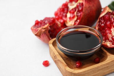 Photo of Tasty pomegranate sauce in bowl and fruits on light table, closeup. Space for text